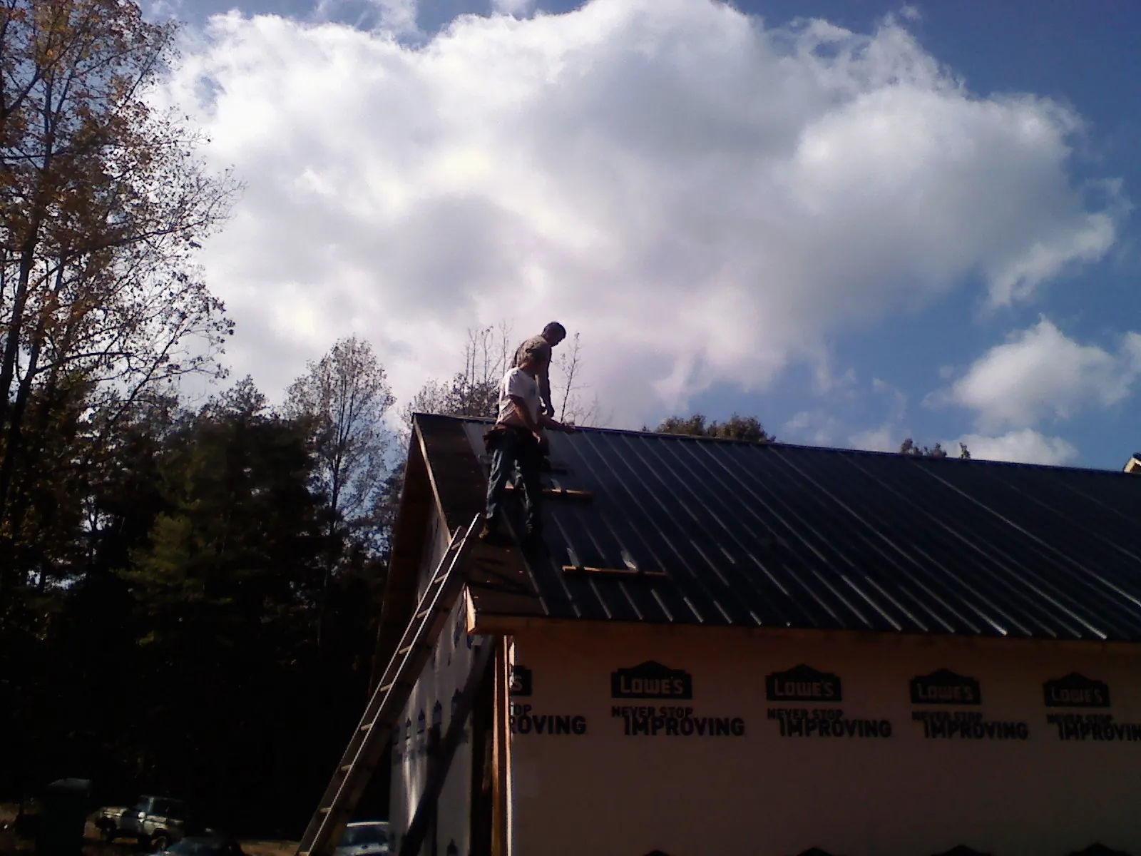 Roofer fastening dark metal panels high against a cloudy sky, from a Roof Inspection job in Corvallis